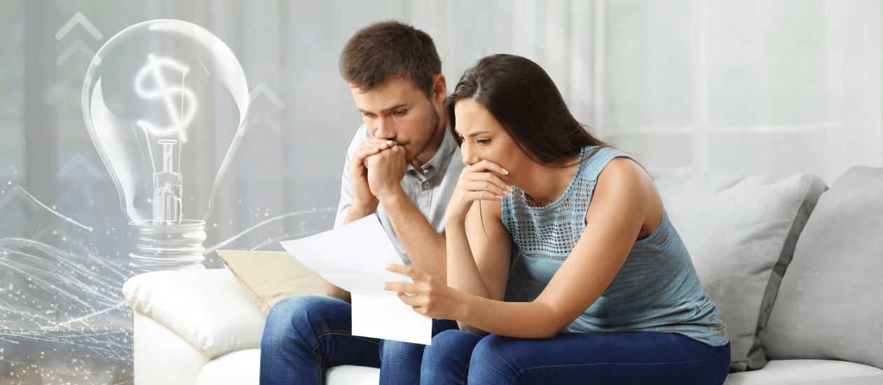 Couple on couch, looking concerningly at their high utility bill