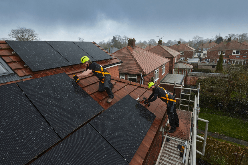 two construction workers installing solar panels on a roof